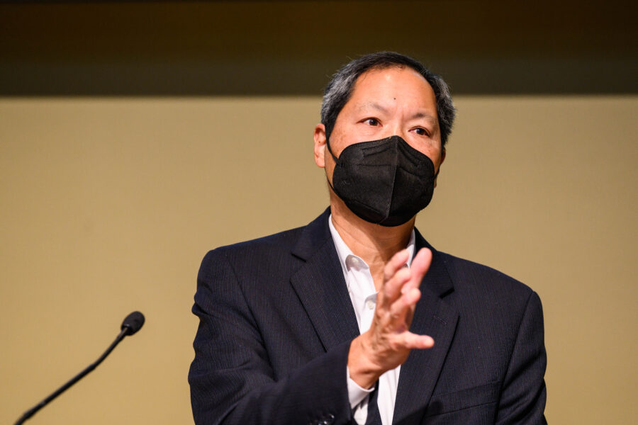 Russell Jeung gestures as he speaks at a lecture wearing a black face mask.