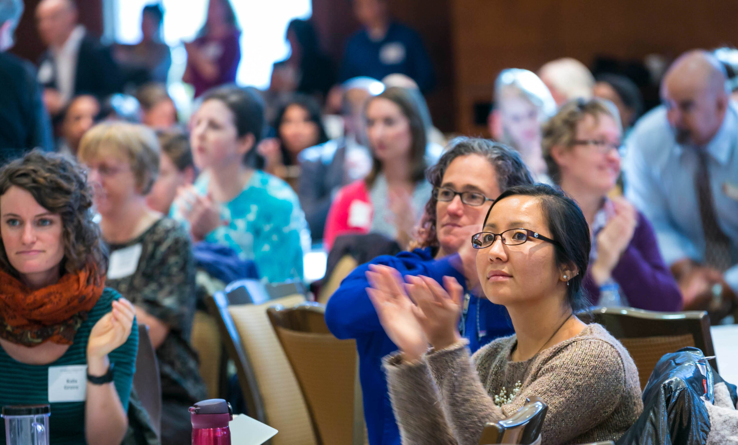 Audience members clapping while sitting at round tables.